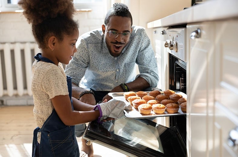 Dad and daughter taking cupcakes out of the oven