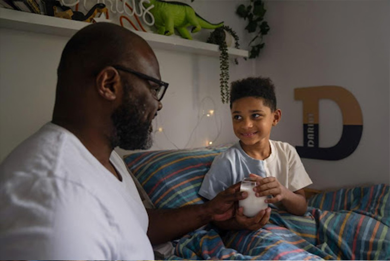 Dad handing a glass of milk to his son in bed