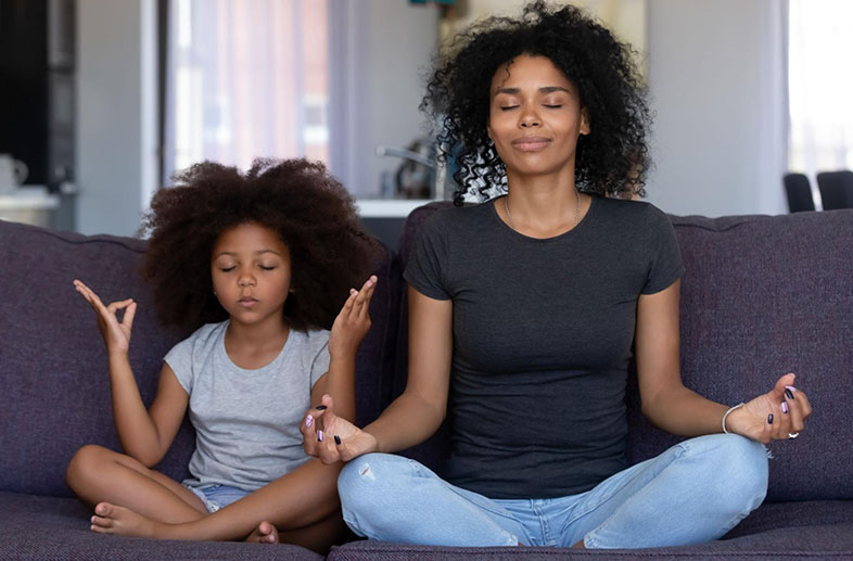 Mom and daughter meditating on a couch