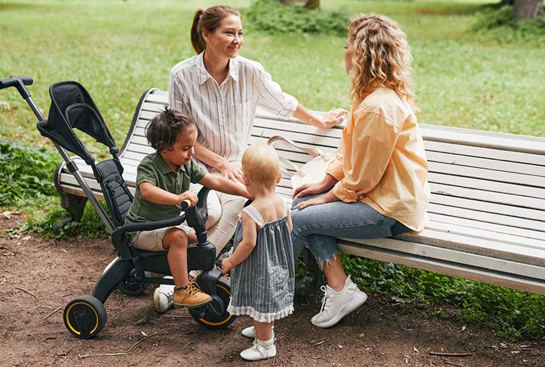 Moms and toddlers relaxing at a park bench