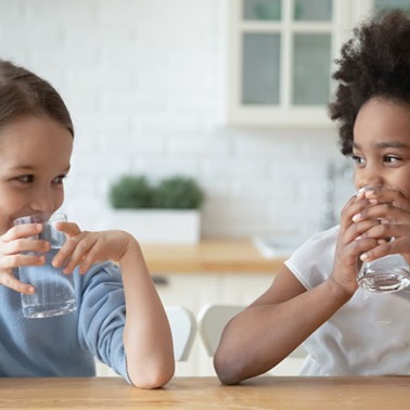 Two smiling girls drinking water at a table