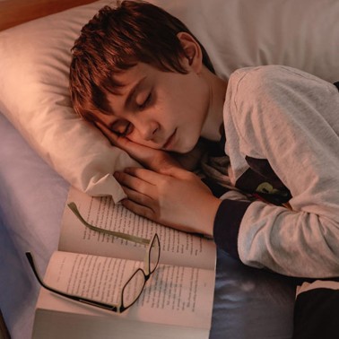 Sleeping boy beside an open book and spectacles