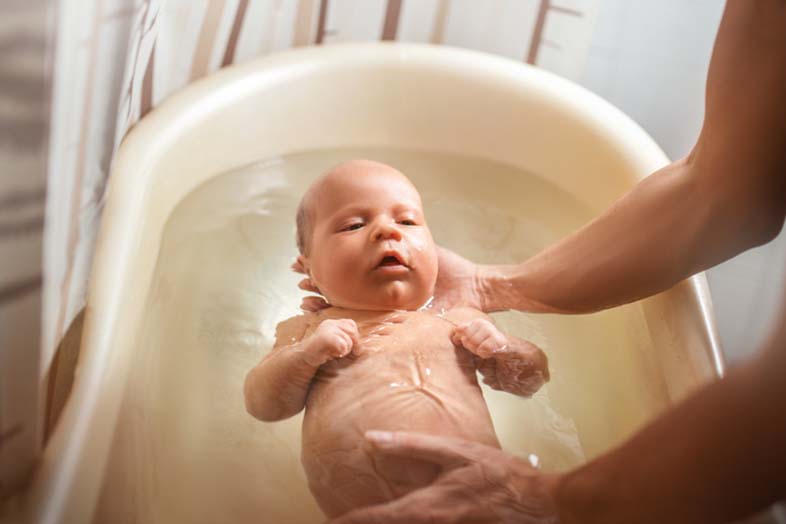 newborn baby being lowered into a plastic bathtub. it is the babys first bath