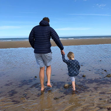 Father and toddler son padding in sea waves.