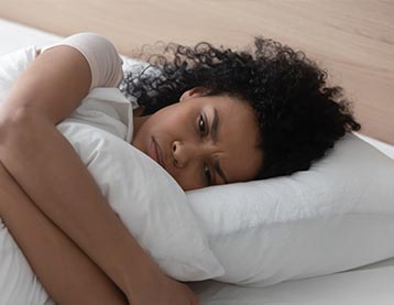 A woman in discomfort lies on her side in bed while holding a pillow